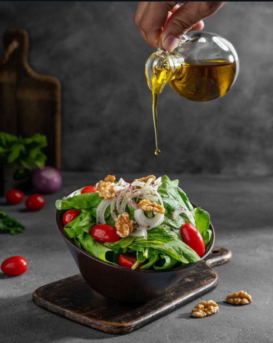 Hand pouring olive oil over a green salad